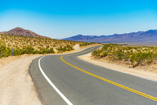 Curved rural road in the Mojave Desert near Barstow, California, with mountains in the background.