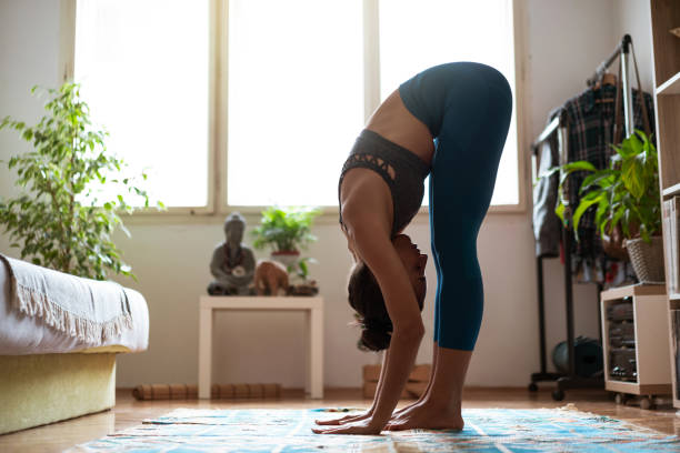 Young Caucasian woman doing yoga at home. She is working on stretching, strength, and body balance.   Practicing meditation and breathing exercise at home.