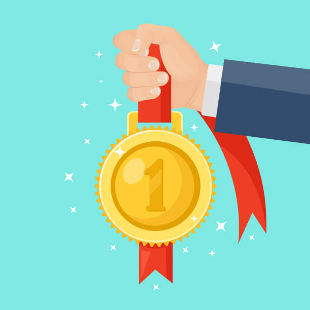 istock Gold medal with red ribbon for first place in hand. Trophy, winner award isolated on background. Golden badge icon. Sport, business achievement, victory concept. Vector flat design 1262776091