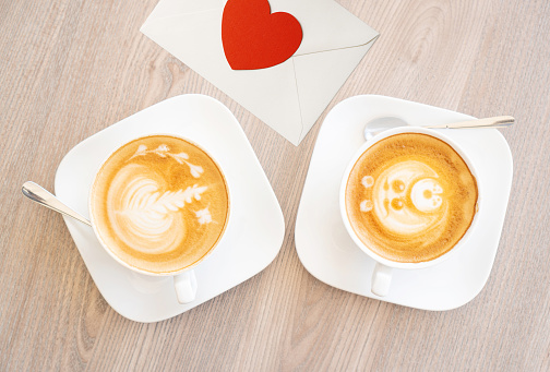 Two white cups of tasty cappucino and valentine letter with heart. Top view. Romantic meeting concept. Wood texture table background.