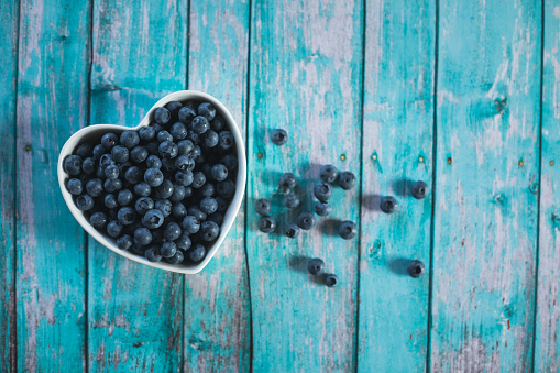 Directly above shot of abundance of fresh blueberries in a heart shaped bowl on a blue wooden table with copy space.