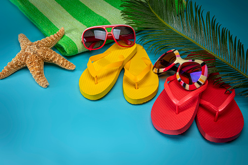 Colored thongs and sunglasses on a blue decking background with copy space