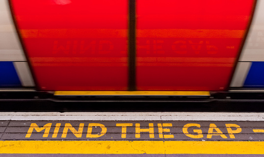 London, England. May 28, 2014. Mind the gap sign with a train moving by it at speed