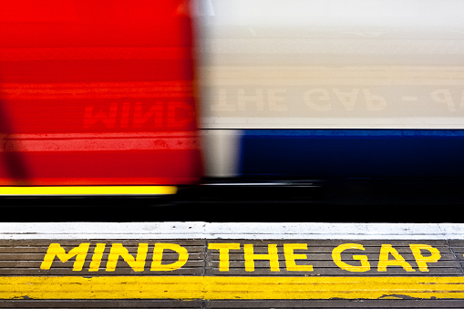 London, England. May 28, 2014. Mind the gap sign with a train moving by it at speed