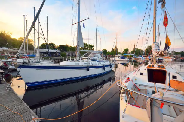 Photo of Elegant and modern sailing boats moored to a pier in a yacht marina at sunset.