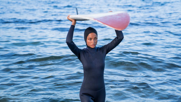 istock Woman with hijab carrying over her head surfboard on beach 1262814292