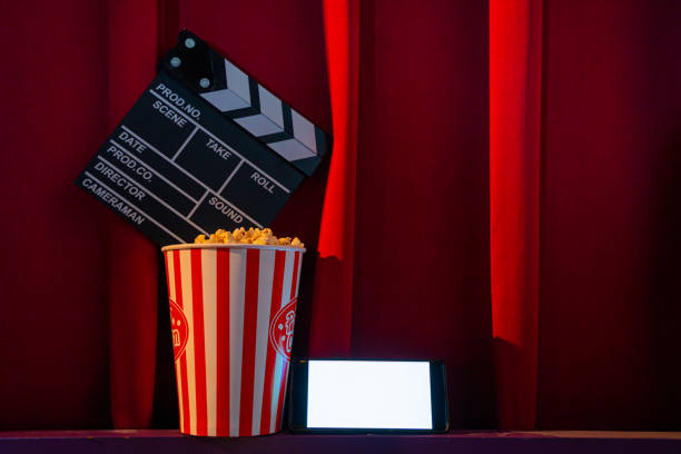 istock mobile phone with empty white bright screen with popcorn bucket and movie clapper board. Concept of streaming TV on internet phone. 1262814835