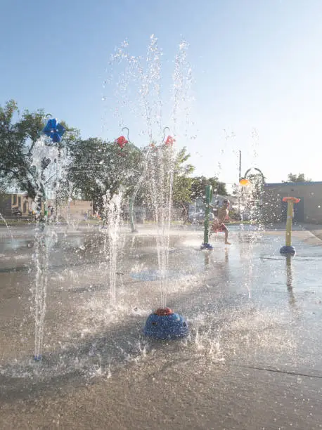 Some kids are playing in the sprinklers at the public water park