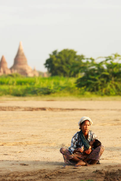 una donna nativa birmana porta con sé un bambino che chiede soldi a un turista che visita un'antica pagoda a bagan, in myanmar. - bagan myanmar burmese culture family foto e immagini stock