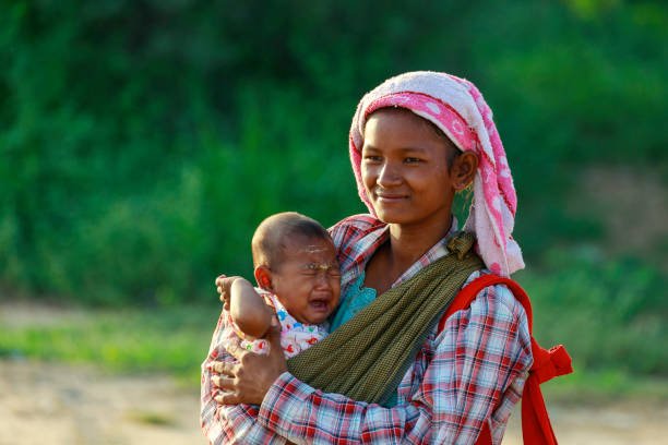 una donna nativa birmana porta con sé un bambino che chiede soldi a un turista che visita un'antica pagoda a bagan, in myanmar. - bagan myanmar burmese culture family foto e immagini stock