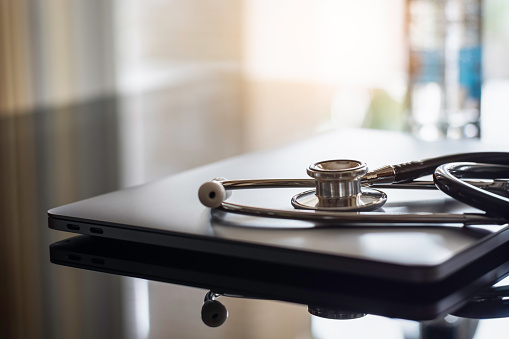 Mockup medical stethoscope and  laptop computer isolated on dark table background with reflection. Medic tech, online medical, emr, telehealth concept.