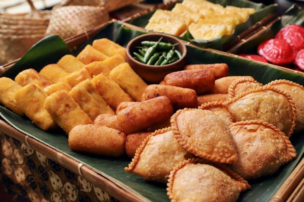 Risoles, Comro and Pastel, Three of Several Indonesian Popular Savory Fritters Risoles, Comro and Pastel, three of several popular Indonesian fritters. Risoles is a Dutch-influenced egg roll; Comro is Sundanese fritter of grated cassava stuffed with oncom soybean; while Pastel is the Peranakan vegetable puff. All the fritters are arranged on a large bamboo tray lined with banana leaf; which then placed on the table together with other snacks. indonesian culture stock pictures, royalty-free photos & images