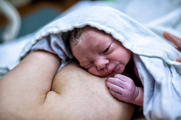 un bebé recién nacido descansa sobre el pecho de su madre y le mira a los ojos por primera vez. - enzo fotografías e imágenes de stock