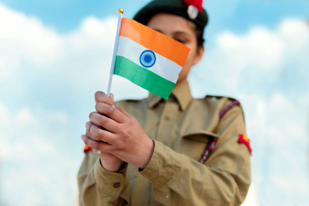 Happy independence day - girl in NCC uniform and holding Indian flag, against blue cloudy sky. outdoor image of an happy Indian girl in NCC uniform, holding Indian flag and celebrating independence day (15 august). indian navy stock pictures, royalty-free photos & images