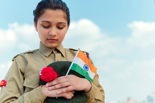 outdoor image of an happy Indian girl in NCC uniform, holding Indian flag and celebrating independence day (15 august).