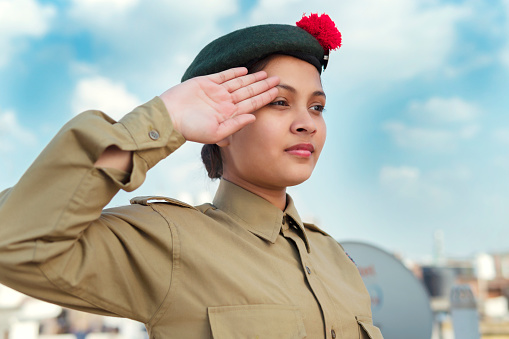 outdoor image of an happy Indian girl in NCC uniform, giving salute against blue cloudy sky and celebrating independence day (15 august).