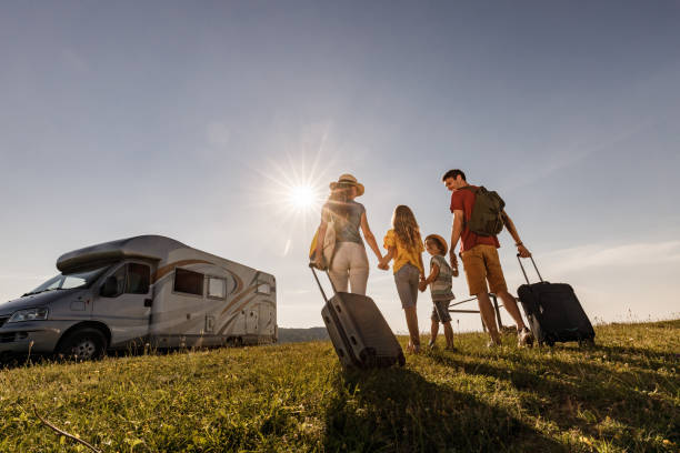 Below view of happy family going on a trip with camp trailer. Low angle view of happy family holding hands while walking towards their camper trailer for a summer vacation. Copy space. rv travel stock pictures, royalty-free photos & images