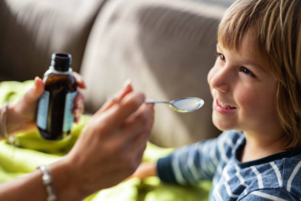 счастливый мальчик, принимающий сироп от кашля от родителей дома. - cough medicine spoon medicine liquid стоковые фото и изображения