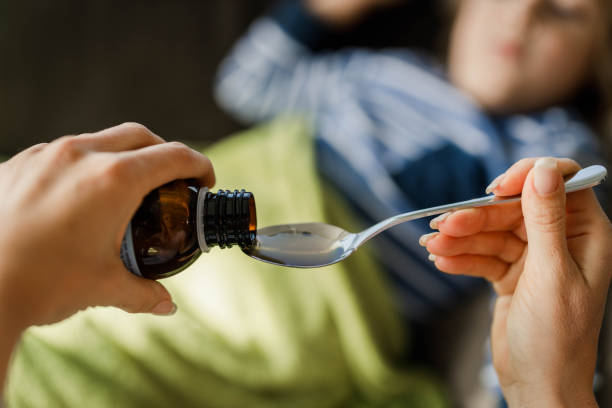 primo di madre irriconoscibile che versa lo sciroppo di tosse nel cucchiaio. - cold remedy foto e immagini stock