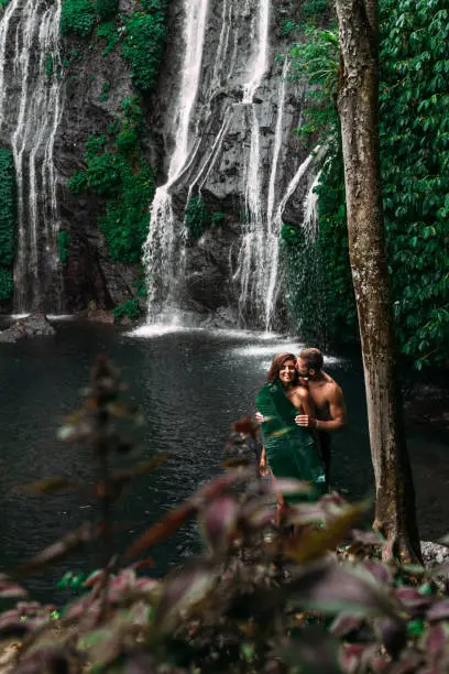 Photo of Lovers at the waterfall. Beautiful couple at a waterfall in Indonesia. A couple in love travels around the island of Bali. A man and a woman kiss at the waterfall. Travel to Asia. Copy space