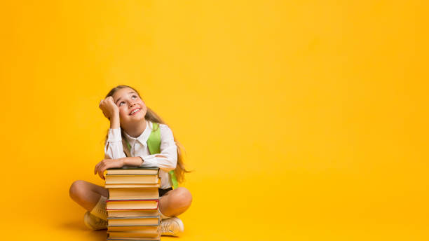 istock Schoolgirl Dreaming Sitting At Books Stack Over Yellow Background, Panorama 1262860633