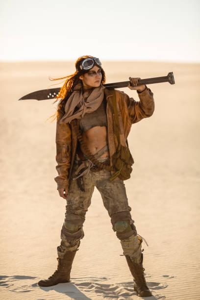Post-apocalyptic Woman Outdoors in a Wasteland Post-apocalyptic woman warrior with weapon outdoors. Attractive fichter girl in shabby clothes holding sword standing in a confident pose looking away. People in nuclear post-apocalypse time. Life after doomsday concept. Desert and dead wasteland on the background. cosplay character stock pictures, royalty-free photos & images
