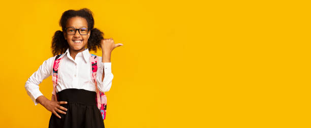 istock School Girl Pointing Thumb Aside Over Yellow Studio Background, Panorama 1262861991
