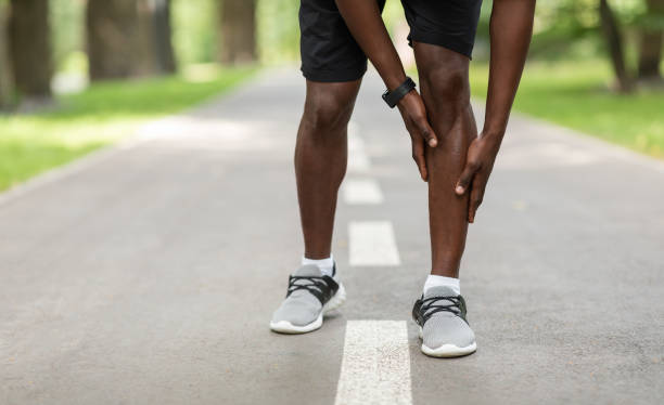 istock Black sportsman touching his aching leg while jogging outdoors 1262862104