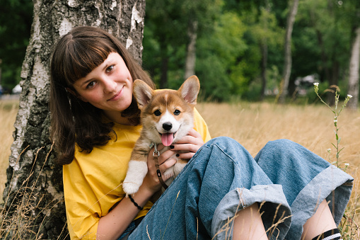 cute teenage girl cuddling a corgi puppy, nature background