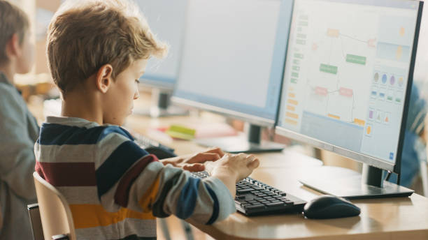 istock Elementary School Computer Science Classroom: Smart Little Schoolboy Works on Personal Computers, Learning Programming Language for Software Coding. Schoolchildren Getting Modern Education 1262866094