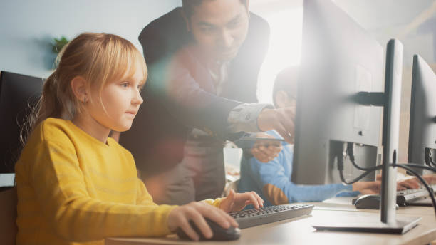 小学校の理科教室:教師は、ソフトウェアコーディングに必要なプログラミング言語を学ぶために、コンピュータを使用する方法をスマートリトル女子高生に説明します。現代教育の進捗状況 - elementary student little boys classroom child ストックフォトと画像