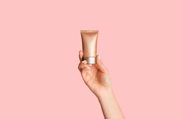 female hand showing bottle of cosmetic foundation on pink background, closeup - moisturizer cosmetics merchandise human hand imagens e fotografias de stock