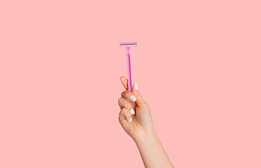 Young girl showing disposable razor on pink background, closeup of hand