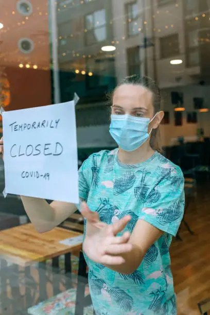 Woman placing a coronavirus closure sign in a coffee shop