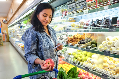 Portrait of an Asian woman putting in an apple into her shopping cart when doing grocery shopping.