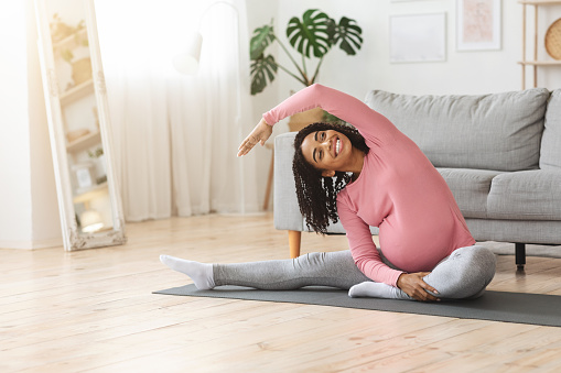 Positive african american pregnant woman doing morning exercise at home, empty space