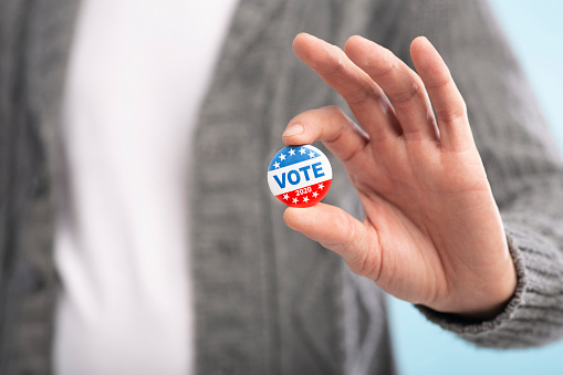 Vote 2020. Law abiding american citizen holding vote button in hand, blurred background