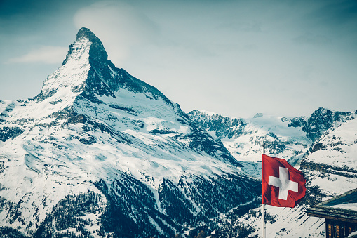 World famous mountain peak Matterhorn above Zermatt town in Mattertal, Valais canton, Switzerland, in winter with Switzerland national flag. Taken by Sony a7R II, 42 Mpix.
