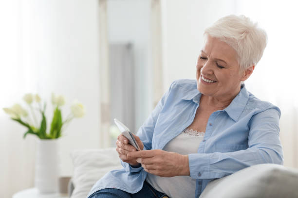 istock Happy elderly lady using mobile phone while relaxing on couch at home 1262878709