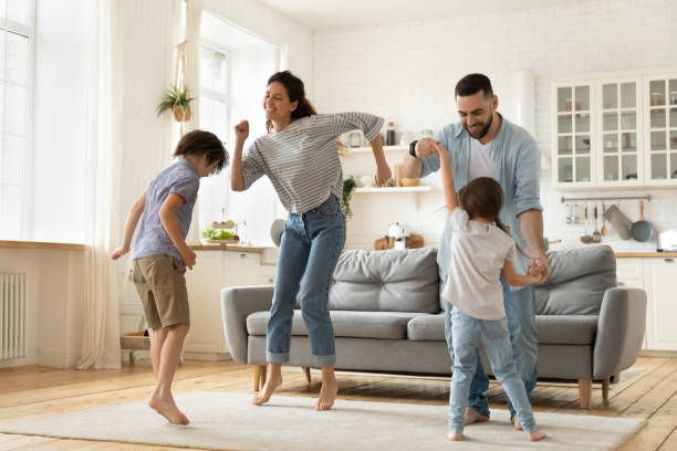 遊び心のある小さな子供たちと踊る興奮した若い夫婦。 - domestic life jumping child sofa ストックフォトと画像