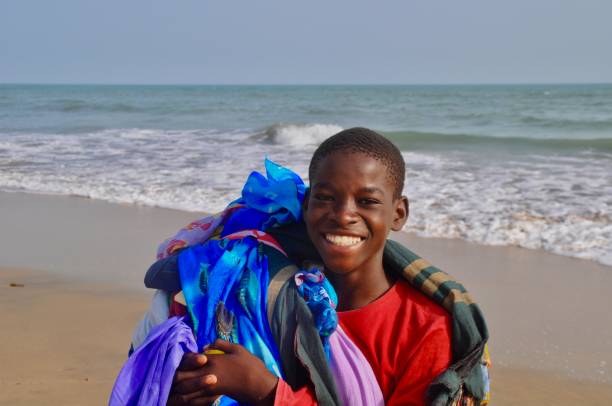 Cute little African boy in swim shorts splashing in the sea during a trip to the beach in summer