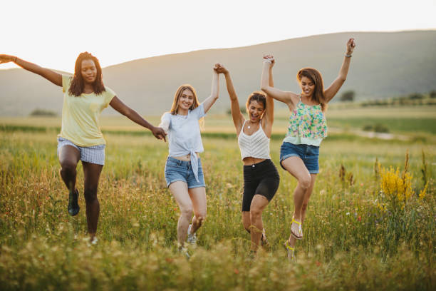 Cheerful girlfriends having fun in nature , running and jumping on flower meadow at beautiful sunny summer day