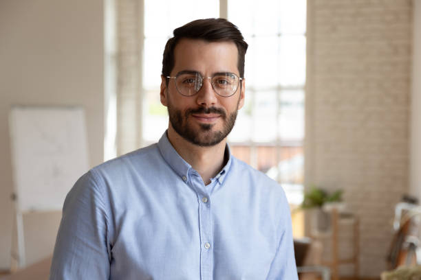 headshot portrait successful businessman standing in office posing for camera - reduction looking at camera finance business imagens e fotografias de stock