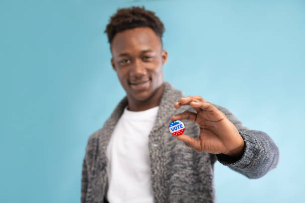 uomo afroamericano con pulsante vota in mano - voting election badge straight pin foto e immagini stock
