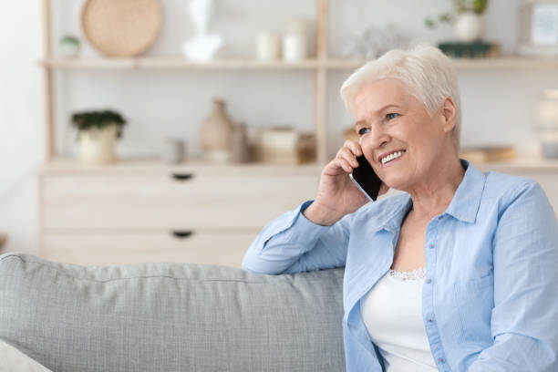 istock Smiling senior lady talking on cellphone while relaxing on couch at home 1262891416