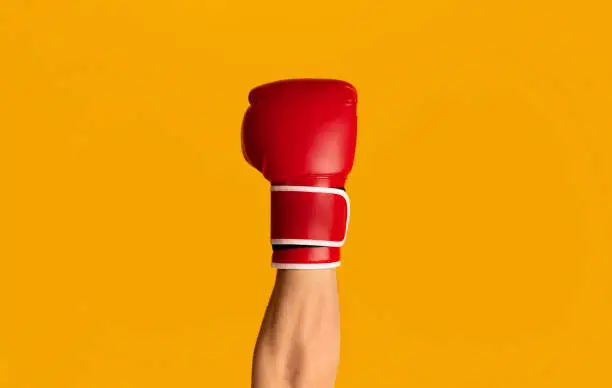 Sportsman wearing boxing glove over orange background, closeup of hand. Panorama
