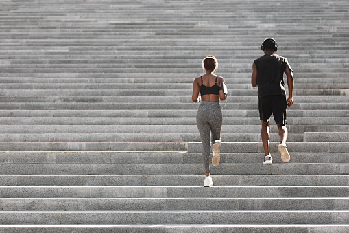 Outdoor sport concept. Rear view of black couple running up on stairs in city park, copy space
