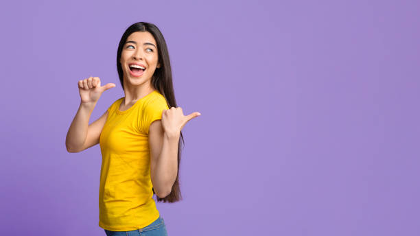 istock Joyful asian girl pointing on copy space behind her back with thumbs 1262893161
