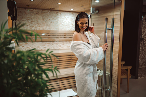 Cheerful and smiling young woman wearing a bathrobe relaxing and resting in the sauna