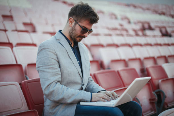 istock Man sitting in the empty soccer stadium and using a laptop 1262893388